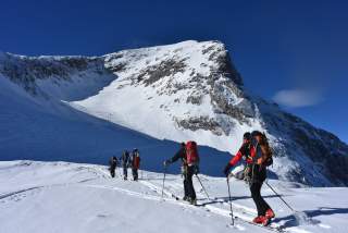 5 Skibergsteiger*innen beim Aufstieg mit Ski vor einem Gipfel