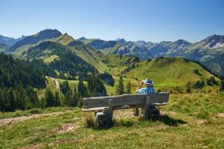 Ein Mann sitzt auf einer Bank und genießt das Panorama in den Tannheimer Bergen/Tirol.