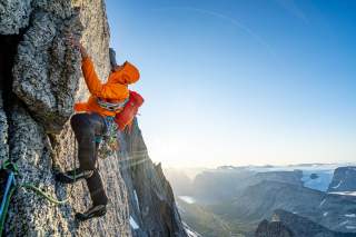 Mann klettert an steiler Felswand vor Aussicht über Grönland