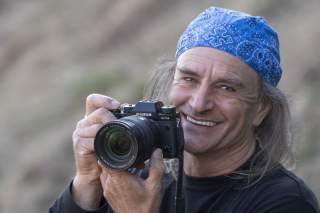 Mann mit langen Haaren und blauer Mütze hält Kamera in der Hand