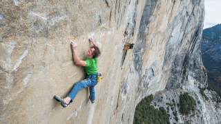 Mann klettert weit oben in steiler Felswand