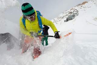 Man gräbt mit Lawinenschaufel im Schnee