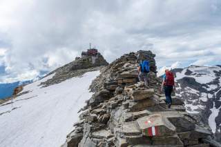 Zwei Menschen wandern über Blockgelände auf Hütte zu