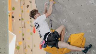 Wettkampfkletterer in weißem T-Shirt an künstlicher Kletterwand nach oben.