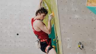 Kletterer in rotem Tanktop greift ein Fingerlock an künstlicher Kletterwand.