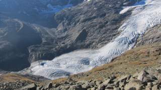 Gletscher in einem felsigen Hochgebirgstal mit sichtbaren Gletscherspalten und Geröll im Vordergrund.