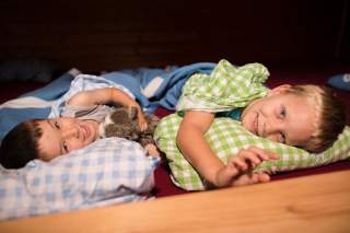 Zwei Kinder liegen in Matratzenlager in Hütte