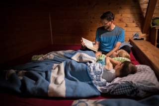 Mann liest Kindern Geschichte in Matratzenlager auf Hütte vor