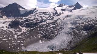 Schneebedeckte Berge mit Gletscher und Felsflächen unter blauem Himmel.