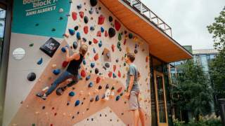 Frau klettert an Boulderwand, Mann steht daneben