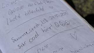 Handschriftliche Einträge in einem Gipfelbuch mit Namen, Grüßen, Smileys und einem Herzsymbol.