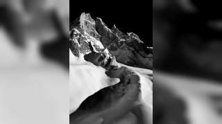 Schneebedeckte, zerklüftete Berggipfel vor schwarzem Himmel in Schwarz-Weiß.