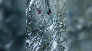 Mehrere Bergsteiger klettern mit Seilen und Ausrüstung an einer steilen, verschneiten Felswand.