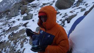 Person isst Expeditionsessen vor schneebedecktem Hang.
