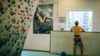 Alex Megos von hinten stehend in einer Kletterhalle