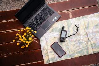 Auf einem Tisch liegen Karte, Smartphone, Laptop und GPS-Gerät