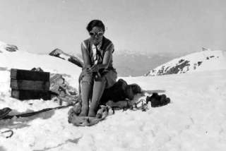 Historisches Foto von Frau, die auf einem verschneiten Berg auf Rucksack sitzt