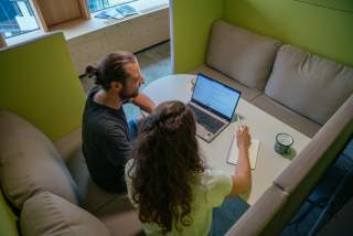 Zwei Personen sitzen vor Laptop und arbeiten