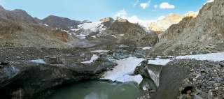 Blick auf eine Gletscherzunge, die in einen See ausläuft, umgeben von Toteisscherfeld im Hochgebirge