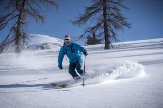 Skifahren bei einer sanften Abfahrt im Pulverschnee fährt direkt auf die Kamera zu.
