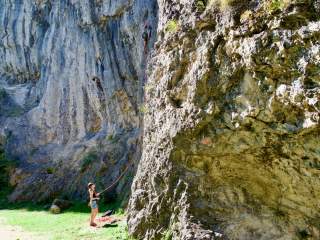 Zwei Personen beim Klettern: eine klettert an einer steilen Felswand, die andere sichert den Aufstieg mit einem Seil von unten.