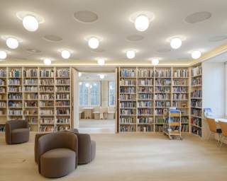 Blick in einen Bibliothektsraum: viel Holz, ein großes Bücherregal an der Wand, im Raum mehrere Polstersessel zum Lesen.