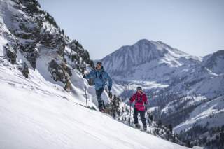 Zwei Personen befinden sich im Anstieg auf einer Skitour im freien Gelände. Im Hintergrund die Bergkulisse.