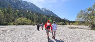 Eine Gruppe Menschen wandert in einem trockenen Flussbett vor einer Bergkette.