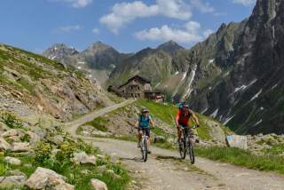 Zwei Menschen fahren auf Mountainbikes von Hütte weg