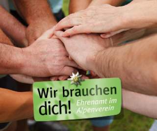 Mehrere Hände liegen übereinander, symbolisieren Zusammenhalt, mit dem Text „Wir brauchen dich! Ehrenamt im Alpenverein“.