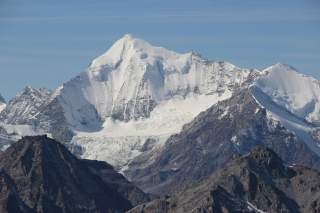 Schneebedeckte Berggipfel vor klarem, blauem Himmel, mit darunterliegenden dunklen Felsformationen.