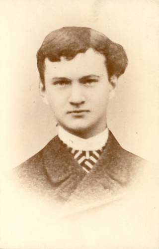 Historisches Schwarz-weiß-Porträt eines jungen Mannes mit kurzen, leicht welligen Haaren, der einen Anzug und eine gestreifte Krawatte trägt.