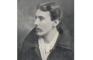 Schwarz-weiß-Porträt eines Mannes mit Schnurrbart in seitlicher Ansicht, bekleidet mit dunklem, derben Mantel und hellem, dünnen Schal.