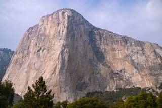 Große, steile Big-Wall-Wand mit glatter, hellgrauer Oberfläche und dunklen Schattenstellen, darunter grüner Wald.