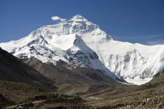 Schneebedeckter Mount Everest unter blauem Himmel, im Vordergrund felsiges, karges Gelände.