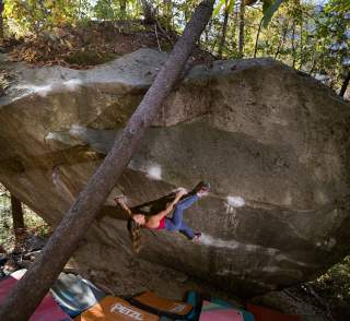 Eine Frau klettert an einer steilen Felswand im Freien, unter ihr liegen mehrere Bouldermatten.