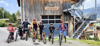 Drei Erwachsene und vier Kinder auf Mountainbikes vor Holzgebäude