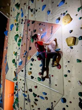 Mann klettert mit Stirnlampe in einer dunklen Kletterhalle Mann klettert mit Stirnlampe in einer dunklen Kletterhalle
