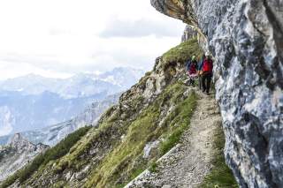 Einsatz im steilen Gelände: Einsatzkräfte der Bergwacht Bayern transportieren eine verletzte Person mit der Gebirgstrage über einen schmalen Bergweg – oft sind Rettungen im alpinen Gelände nur zu Fuß möglich.