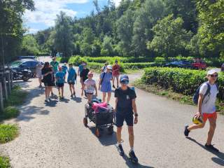 Eine Gruppe Kinder und Jugendliche läuft an einem Sommertag mit einem Bollerwagen auf einem Schotterweg.