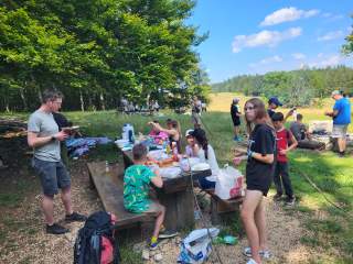 Eine Gruppe Jugendlicher und Kinder auf einem Picknickplatz in der Natur.