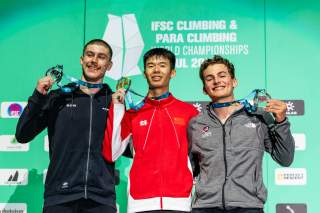 Drei Kletterer stehen vor einer grünen Wand mit der Aufschrift 