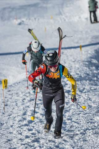 Ein Skibergsteiger beim Sprint im Aufstieg mit Ski auf dem Rücken und im Hintergrund ein österreichischer Athlet
