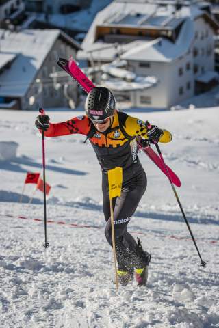 Ein Skibergsteiger beim Sprint im Aufstieg mit Ski auf dem Rücken und im Hintergrund eine Liftstation