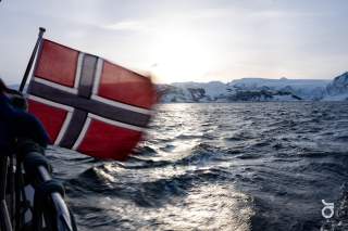 Norwegische Flagge auf einem Boot über dem Meer. Im Hintergrund verschneite Berge.
