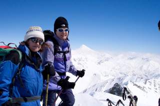 Zwei Skitourengeherinnen mit schneebedeckten Gipfeln im Hintergrund