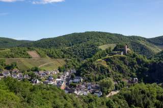 Blick auf Dörfchen mit Burg und bewaldeten Hügeln
