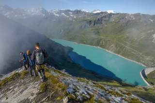 Drei Wandernde oberhalb eines türkisen Stausees