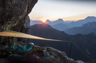 Dörte Pietron liegt im Schlafsack in einem Biwak mit Aussicht auf den Sonnenuntergang über den Dolomiten.