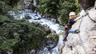 Kleines Kind hängt im Klettersteig, daneben der Blick in die Schlucht.